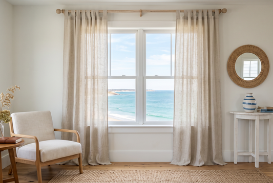Coastal living room with sheer linen curtains at a window overlooking the sea