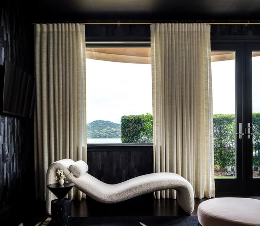 Living room with cream floor-length curtains and sheers framing tall windows beside a white chaise