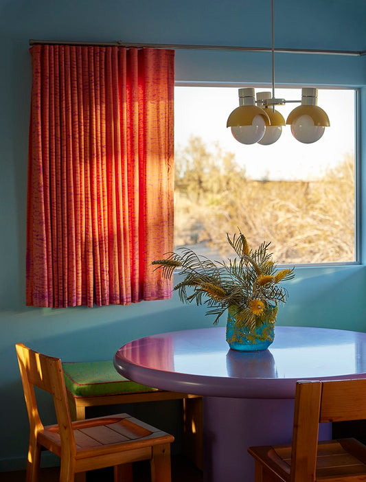 Dining nook with sill-length red curtains on a window above a round table