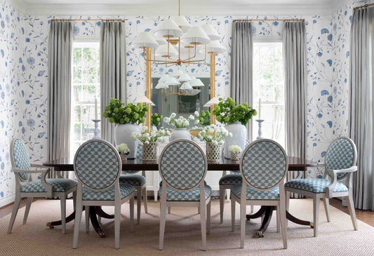 Dining room with gray curtains framing tall windows, floral wallpaper and blue upholstered chairs