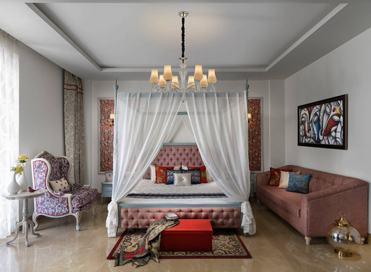 Four-poster canopy bed with white sheer curtains under a chandelier in a pink and red bedroom
