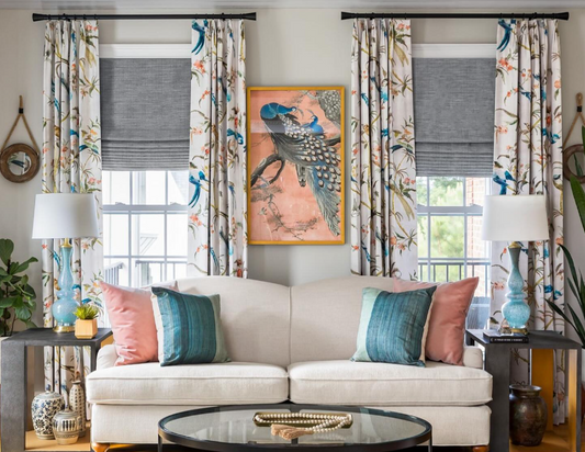 Living room with floral print curtains layered over blue roman shades behind a cream sofa